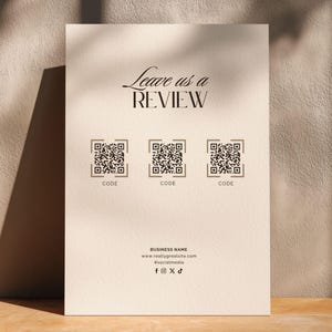 Puede incluir: Un letrero rectangular de color beige con el texto Leave us a REVIEW en fuente negra. Debajo hay tres códigos QR cuadrados, cada uno etiquetado como CODE. En la parte inferior, el texto BUSINESS NAME, una URL, un usuario y cuatro iconos.
