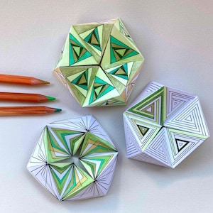 May include: Three geometric paper sculptures featuring intricate triangular patterns in shades of green, yellow, and white, accompanied by three orange-colored pencils. The paper objects display complex line work and folded, multi-faceted surfaces.