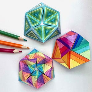 Puede incluir: Tres esculturas geométricas de papel con patrones triangulares coloridos. Una es azul y verde, otra es de color arcoíris, y la tercera es una mezcla de naranja, morado y amarillo. Lápices de colores en verde, naranja y rojo en el fondo.