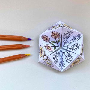 May include: A paper fortune teller featuring floral illustrations of daisies and pansies, with some sections colored in pink, yellow, and purple, and others left as black and white line art, accompanied by three wooden colored pencils.