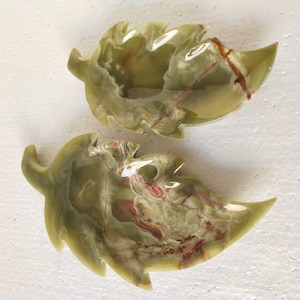 May include: Two green onyx leaf-shaped dishes with intricate patterns. The dishes are carved from green onyx with brown and red veins.