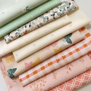 May include: A stack of folded fabric bolts featuring various patterns including white daisies on light green, abstract gray and pink shapes, cream with dandelion prints, butterflies in yellow and teal, pink gingham, and floral sprigs on light pink.