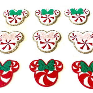 May include: Nine embroidered iron-on patches in the shape of Mickey Mouse ears. The patches feature a red and white candy cane design with a green bow on top. Three patches have a pink bow, three have a green bow, and three have a red bow.