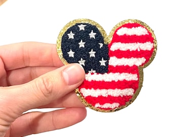 May include: A red, white and blue American flag in the shape of a Mickey Mouse head with a gold glitter outline.