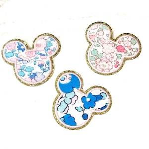 May include: Three fabric Mickey Mouse head appliques with gold trim. The appliques are in pink and blue floral patterns.