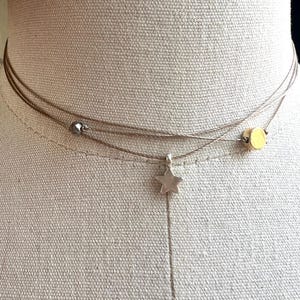 May include: A layered necklace with three strands. The top strand has a small, round, silver bead and a gold-colored bead. The middle strand has a small, silver star pendant. The necklace is displayed on a mannequin.