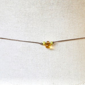 May include: A simple brown cord necklace with a single amber bead and two smaller green beads.