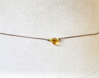 May include: A simple brown cord necklace with a single amber bead and two smaller green beads.