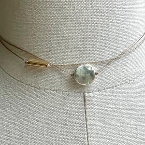 May include: Two-strand necklace with a delicate design. The top strand features a small, gold-colored bar. The bottom strand has a silver-colored, irregularly shaped pendant. The necklace is displayed on a neutral-colored mannequin.