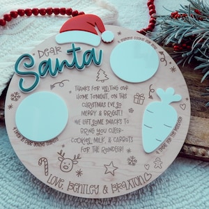 May include: A circular wooden Christmas Eve plate with the words "Dear Santa" and a Santa hat. It has spaces for cookies, milk, and carrots, with the message "Love, Bentley & Braxton". Decorative elements include a carrot, reindeer, and snowflakes.