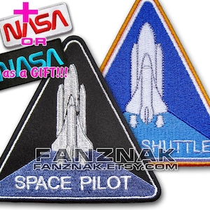 May include: Embroidered patches with a space shuttle design. One patch is black with white text reading "SPACE PILOT" and "FANZNAK.ETSY.COM". Another patch is blue with "SHUTTLE" text. Additional patches with "NASA" text are also visible.