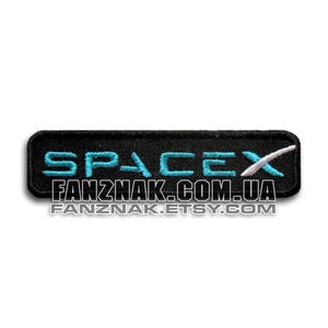 May include: Black embroidered patch with the word "SPACEX" in turquoise, a white stylized "X", and the text "FANZNAK.COM.UA" and "FANZNAK.ETSY.COM" in white. The patch is rectangular.
