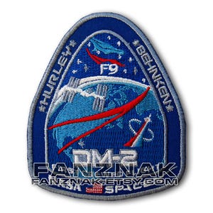 May include: A blue and white embroidered patch with the text "Hurley" and "Behnken" on the left and right sides, respectively. The patch also features a red and white rocket, a blue and white globe, and the text "DM-2" and "F9".