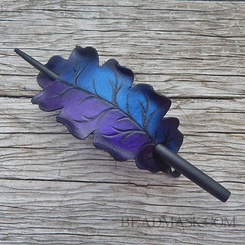 A purple and blue leather leaf hair clip with a black wooden stick. The leaf is embossed with a vein pattern.