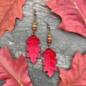 Peut inclure: Boucles d'oreilles artisanales avec des pendentifs en forme de feuilles rouges. Les boucles d'oreilles ont des crochets cuivr&eacute;s et de petites perles aux tons terreux. Les feuilles sont d&eacute;taill&eacute;es avec des motifs de veines. Th&egrave;me automnal.