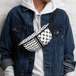 May include: A person wearing a white hoodie, a blue denim jacket, and white pants. They are wearing a black and white fanny pack with a geometric pattern.