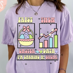 以下が含まれることがあります： 「First Then Easter Data I'm Earning a Break」のテキストが入った、蘭色の紫色のTシャツ。グラフィックはイースターバスケットと、上向きの矢印が付いたデータチャートが特徴です。ゆったりとしたフィット感のシャツです。