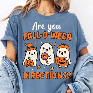 Könnte beinhalten: Ein blaues T-Shirt mit dem Text "Are you FALL-O-WEEN DIRECTIONS?" und drei Cartoon-Geistern. Ein Geist trägt einen Hexenhut und hält einen Kürbis, ein anderer hält einen Lolli, und der dritte trägt einen Kürbishut und hält einen Kürbis.