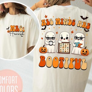 Op de afbeelding: Crèmekleurig T-shirt met Halloween-thema graphics. De voorkant heeft "Mrs. Hannah" in oranje en zwarte letters. De achterkant toont geesten, pompoenen, vleermuizen en de tekst "All Minds Are BOOTIFUL" in oranje en bruin.
