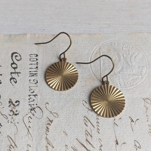 Puede incluir: Un par de pendientes de color dorado con un diseño de rayos de sol. Los pendientes están hechos de metal y tienen un cierre simple de gancho.