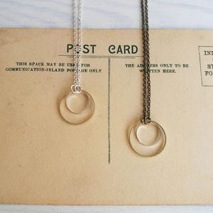 May include: Two gold necklaces with a double circle pendant design. One necklace has a silver chain and the other has a bronze chain.