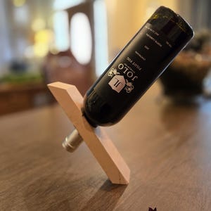 May include: A wooden wine bottle holder with a bottle of Jolo Pinot Noir wine resting on it. The bottle is resting on the holder at an angle, with the label facing the camera. The label reads "Jolo Pinot Noir, Alexander Valley, California".