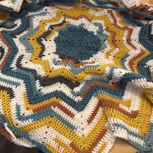 May include: A crocheted blanket with a starburst pattern in shades of white, yellow, brown, and blue.