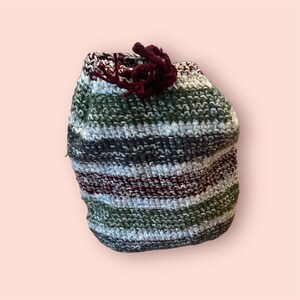May include: A striped crocheted bag with a burgundy tassel. The bag is made with green, white, and gray yarn.