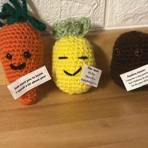 May include: Three crocheted stuffed vegetables with embroidered faces and motivational messages. A carrot with the message "Just want you to know I carrot a lot about you!" A pineapple with the message "Fine-Apple It's fine You're fine Everything's fine" and a brown potato with the message "Positive Potato I may be a tiny potato, but I believe in you. Go do your thing!"
