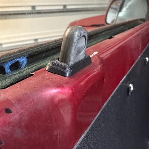 Puede incluir: Primer plano de un pestillo de puerta de coche negro montado en una puerta roja. Se ve un panel interior negro y un espejo retrovisor en el fondo.