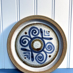 May include: A ceramic plate with a brown rim and a white center. The plate has a blue and brown design of swirls and leaves.
