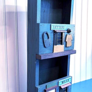 May include: A blue wooden mail organizer with three compartments labeled "Letters", "Bills", and "Mail". The organizer is decorated with a sign that says "Post Office" and has a small window and door.