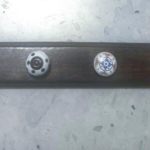 May include: A dark brown wooden wall-mounted coat rack with four decorative knobs. The knobs include a white bird-shaped knob, a black and white patterned knob, a blue and white floral knob, and a clear, flower-shaped knob.