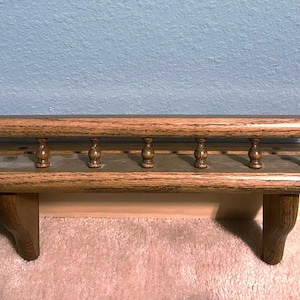 May include: A wooden shelf with a decorative railing and two brackets. The shelf is stained a dark brown color and has a natural wood grain.