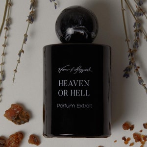 May include: A black bottle of perfume with a black cap and a white label. The label reads "Man & Haggard Heaven or Hell Parfum Extrait".