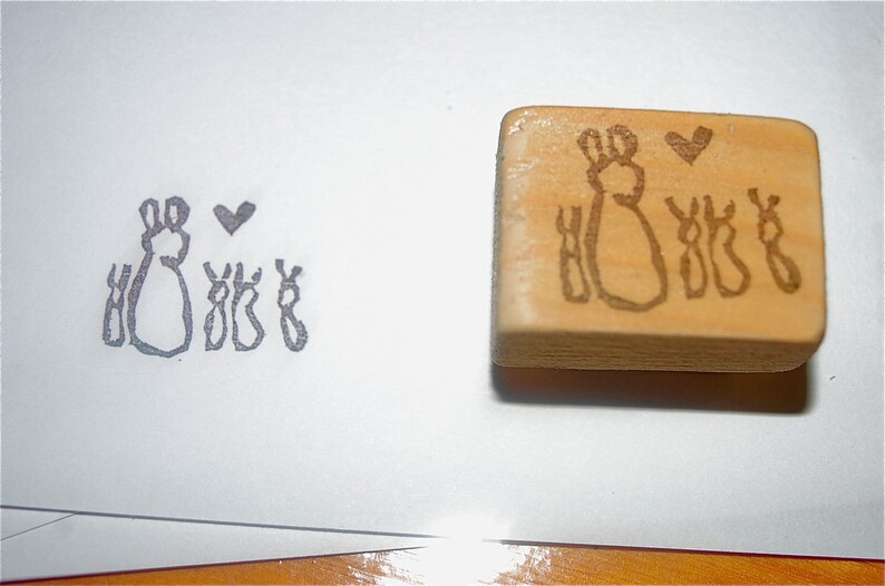May include: A wooden stamp with a design of two bunnies and three baby bunnies with a heart above them.