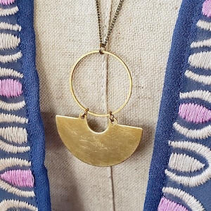 May include: A gold necklace with a large, round pendant and a smaller, crescent-shaped pendant. The necklace is on a mannequin wearing a blue and white patterned shirt.