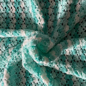 Pode incluir: Um cobertor de bebé em crochê em um esquema de cores azul claro e branco. O cobertor é feito com um ponto texturizado que cria um padrão em relevo.