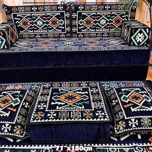 Puede incluir: Un juego de sofás azul marino con cojines estampados y una alfombra a juego. El sofá mide 190 cm de largo y 40 cm de alto. Los cojines y la alfombra presentan diseños geométricos en naranja, verde y blanco.