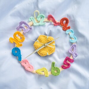 Può includere: Un orologio fatto a mano all'uncinetto con un centro giallo e numeri colorati. I numeri sono in vari colori, tra cui blu, verde, arancione e rosa. Le lancette dell'orologio sono dorate. L'orologio è su uno sfondo bianco.