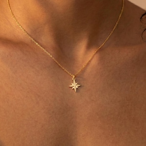 May include: A gold-colored necklace with a starburst pendant. The pendant is a detailed, eight-pointed star. The necklace chain is delicate and thin. The background is a warm, neutral tone, highlighting the jewelry.