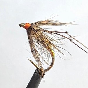May include: A brown and tan fly fishing lure with orange thread and a gold hook.