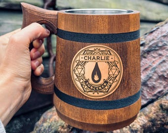 May include: A brown wooden mug with a black band around the top and a metal lid. The mug has a personalized engraved design with the name "Charlie" and the words "Sorcerer" and "D&D".