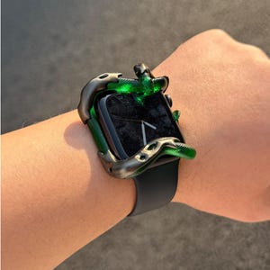 May include: A smartwatch featuring a black screen and a smooth black silicone band, encased in a decorative frame shaped like a metallic dark gray snake with a textured, shimmering green body that coils around the edges of the watch face.