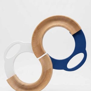 May include: A wooden toy track consisting of two interlocking circular components. One component features a natural wood finish with a white handle, while the other features a natural wood finish with a dark blue handle. The pieces form an S-shape.