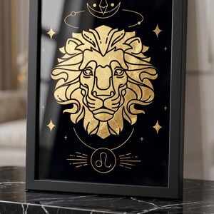 May include: Framed art print featuring a gold lion illustration on a black background. The artwork includes the Leo zodiac symbol and celestial elements. The print is in a black frame and is displayed on a black marble surface.