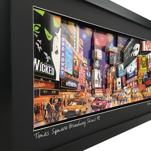 May include: A framed collage of Times Square, New York City, featuring iconic Broadway show posters and a yellow taxi cab. The collage is titled "Times Square Broadway Shows #2".