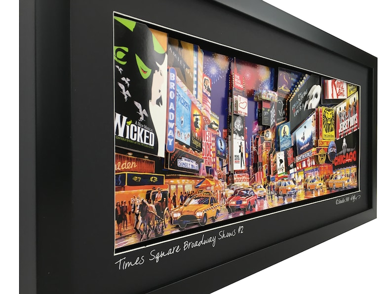 May include: A framed collage of Times Square, New York City, featuring iconic Broadway show posters and a yellow taxi cab. The collage is titled "Times Square Broadway Shows #2".