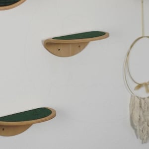 Op de afbeelding: Drie houten kattenplanken met een groene viltbekleding, gemonteerd op een witte muur. De planken zijn gebogen en hebben een afgeronde rand.