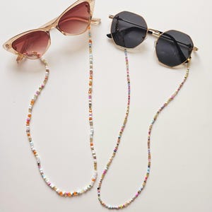 May include: Two pairs of sunglasses with colourful beaded chains. The sunglasses are both gold-toned and have dark lenses. One pair has a cat-eye shape and the other has a square shape.